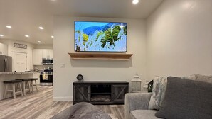 Ein modernes Wohnzimmer mit einem Marmortisch, einem grauen Sofa, einem an der Wand befestigten Flachbildfernseher und einem Deckenventilator.