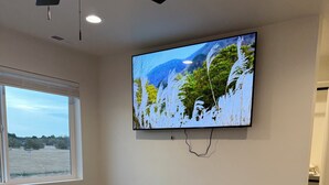 Ein Schlafzimmer mit einem Bett, einem an der Wand befestigten Fernseher, einem Fenster und einem Deckenventilator.
