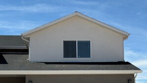 Ein zweistöckiges Haus mit weißer Garagentür, einem kleinen Fenster mit Jalousien und einer steinernen Sockel unter der Tür.