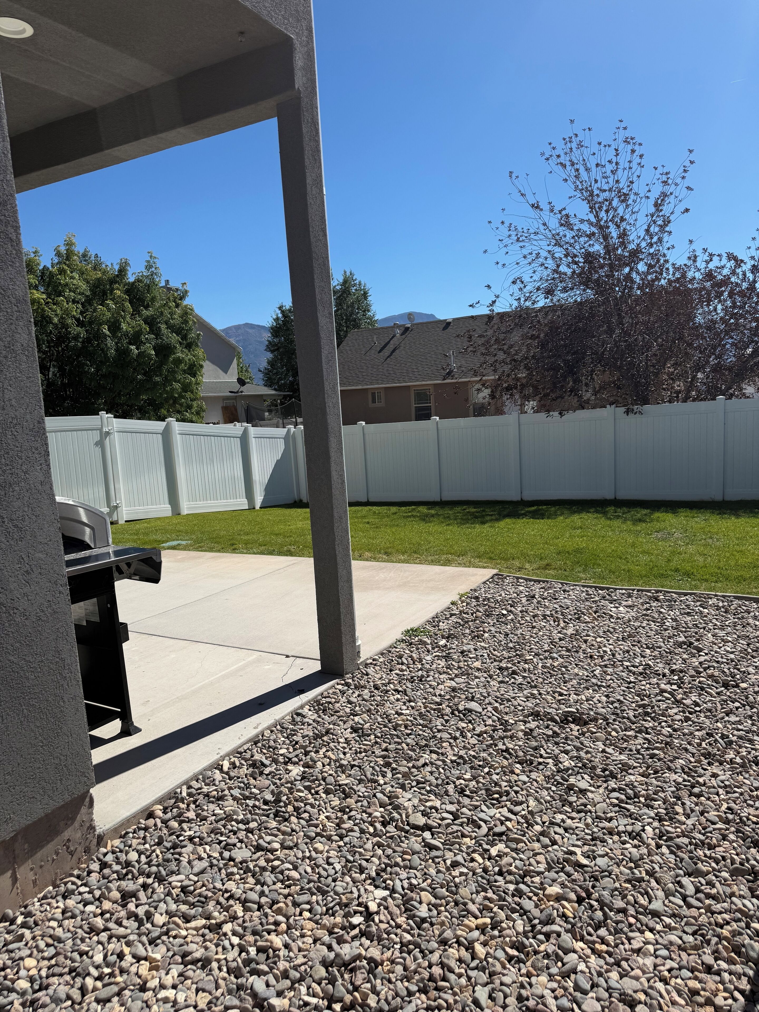 A patio area with a barbecue grill, a white fence, and a gravel ground.