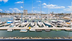 A marina with numerous boats docked in rows, a clear sky, and a building in the background. - Gorgeous Condo | Marina Views | Steps from Harbor Beach 208B (Oceanside)