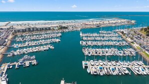 A marina with numerous boats docked, a beach, and a hotel in the background. - Gorgeous Condo | Marina Views | Steps from Harbor Beach 208B (Oceanside)