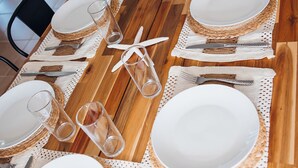 A long wooden dining table set with white plates, cutlery, and glasses, arranged on a wooden floor with chairs around. - Golden Hour Getaway-2 Minutes to Beach, Pool + Arcade, Sleeps 10, (Destin)