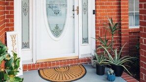 A brick house with a white front door, a doormat, and potted plants. - Golden Hour Getaway-2 Minutes to Beach, Pool + Arcade, Sleeps 10, (Destin)
