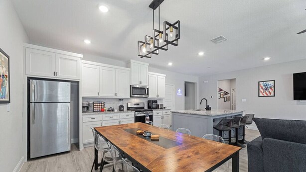 A modern kitchen with white cabinets, stainless steel appliances, and a wooden dining table with chairs. - Sporty Spot - Hot Tub - Walk to AT&T Stadium (Arlington)