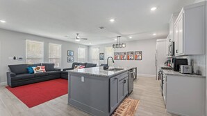 A modern apartment with a grey sofa, red rug, kitchen island, and artwork on the walls. - Sporty Spot - Hot Tub - Walk to AT&T Stadium (Arlington)
