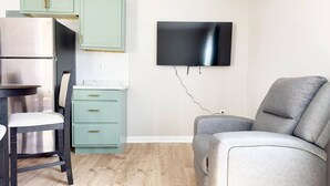 Ett kompakt bostadsutrymme med ett litet kök, en matplats med en stol och en grå soffa.