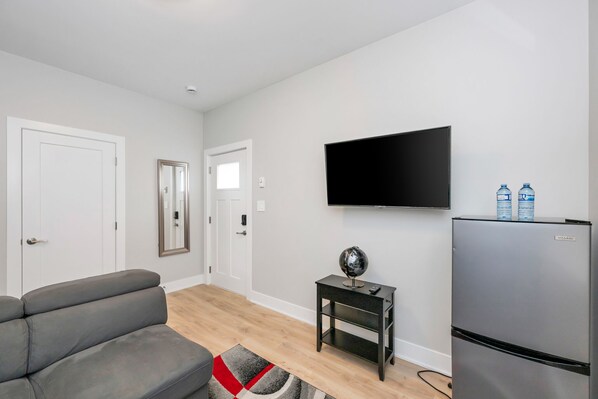 Un salón moderno con un sofá gris, un televisor de pantalla plana montado en la pared, una mesita auxiliar con un globo terráqueo y un refrigerador Vissani.