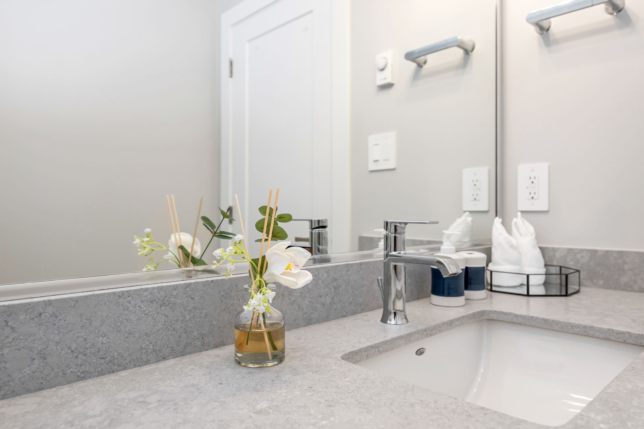 A bathroom with a marble countertop, a sink, a mirror, and a vase with flowers.