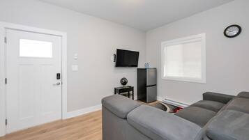Een moderne woonkamer met een grijze modulaire bank, een flatscreen-televisie aan de muur, een tafeltje met een wereldbol en een koelkast.