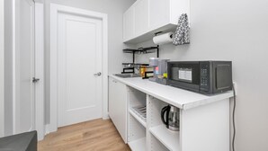 Une cuisine compacte avec des meubles blancs, un four à micro-ondes, une bouilloire et un rouleau d’essuie-tout.