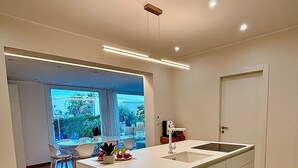 A modern kitchen with a central island, a dining area with chairs, and a view through a glass door. - Villa Sable D'or-Avola (Gallina Beach) just 350 meters from the sea(Sicily) (Gallina)