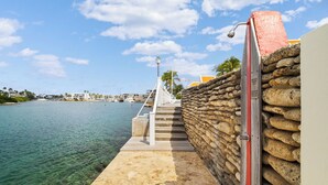 Eine Steintreppe führt zu einer Anlegestelle am Wasser, mit blauem Himmel und Gebäuden in der Ferne.