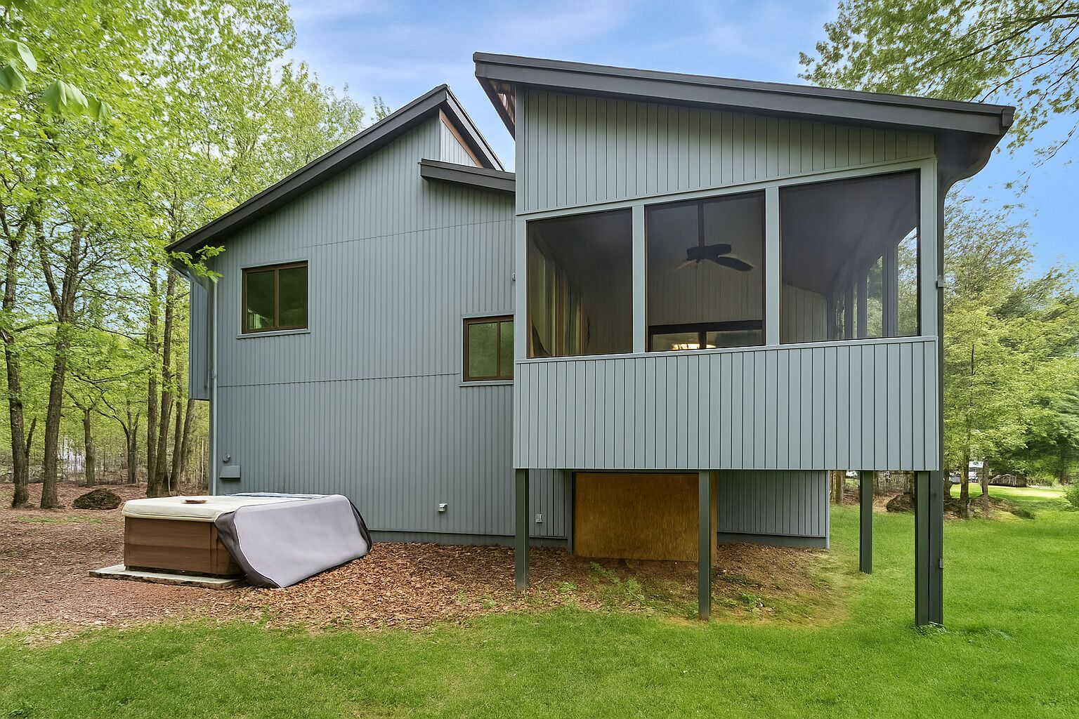 A modern cabin with a loft bedroom, a small outdoor seating area, and a view of the surrounding forest.