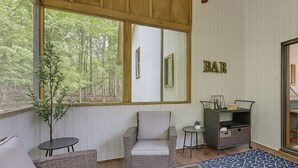 Ein gemütliches Zimmer mit einem großen Fenster, einem Korbstuhl, einem kleinen Tisch und einer Bar.