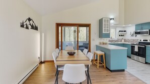 Eine moderne Küche mit türkisfarbenen Schränken, einer zentralen Kochinsel und einem Essbereich mit Holztisch und weißen Stühlen.
