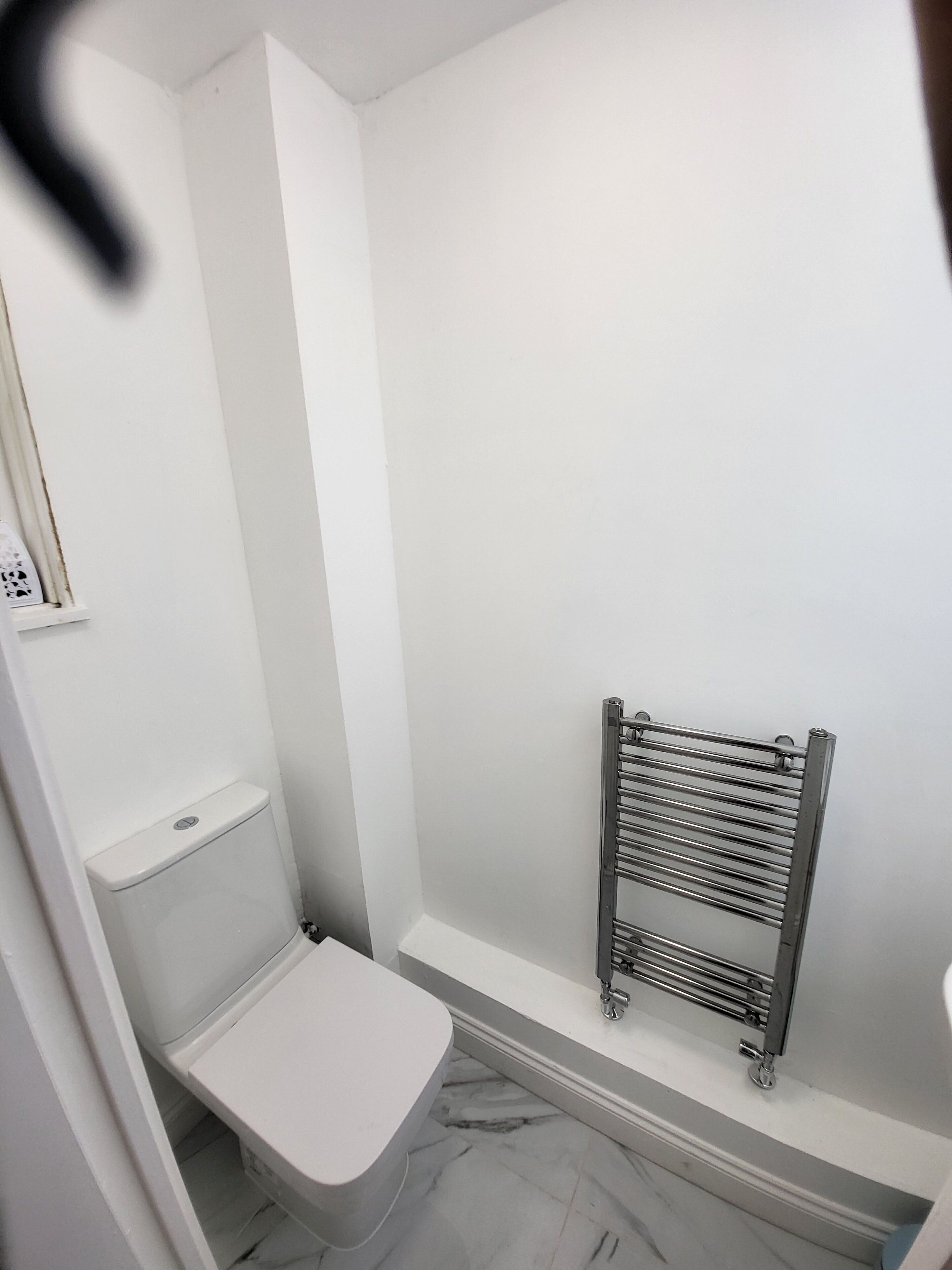 A small, white bathroom with a toilet, a shower, and a towel rack.