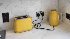 Une cuisine avec un plan de travail blanc, un grille-pain jaune, une bouilloire jaune et divers ustensiles de cuisine rangés sur une étagère.