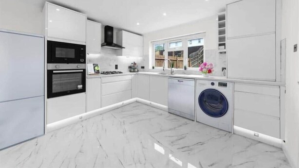 Une cuisine moderne avec des meubles blancs, un four encastré, un four à micro-ondes et un lave-vaisselle.