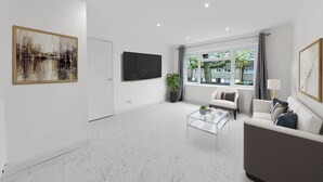 Un salon moderne avec une grande fenêtre, un téléviseur à écran plat, un canapé, une table basse et un tableau accroché au mur.