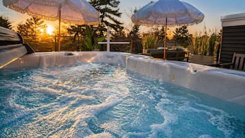 A hot tub with two umbrellas, surrounded by outdoor furniture and trees.