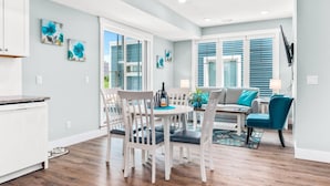 Una cocina moderna con armarios blancos, un comedor con mesa y sillas blancas, y una sala de estar con sofá y sillas color turquesa.