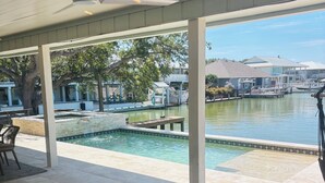 Un espacio al aire libre techado con piscina, sillones de descanso y vista a un puerto deportivo.