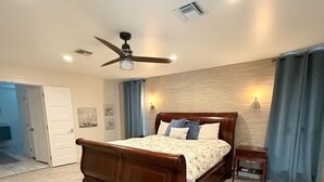 Un dormitorio amplio con una cama grande, un ventilador de techo y una mesita de noche.