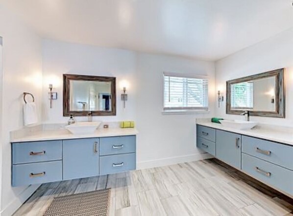 A bathroom with two sinks, blue cabinets, and a large mirror.