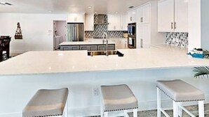 Una cocina moderna con armarios blancos, una isla central y tres taburetes de bar.