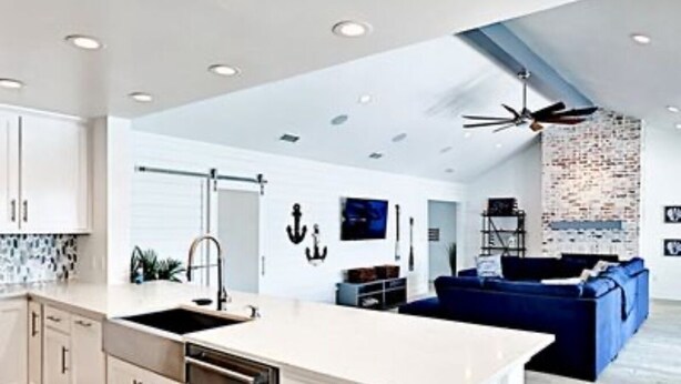 Una cocina moderna con armarios blancos, una isla central y un sofá azul en la zona de estar.