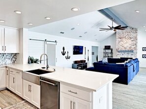 A modern kitchen with white cabinetry, a central island, and a blue sofa in the living area.