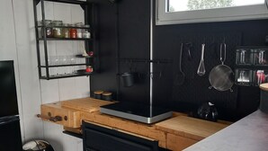 A compact kitchen with a black countertop, wooden drawers, a black trash bin, and a window providing natural light.