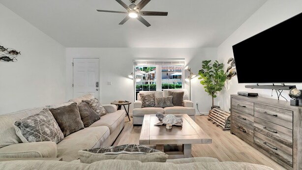 Een moderne woonkamer met een plafondventilator, een bank, een salontafel en een tv op een houten kast.