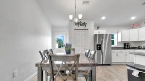 Een moderne keuken met witte kasten, een roestvrijstalen koelkast en een eethoek met een houten tafel en stoelen.