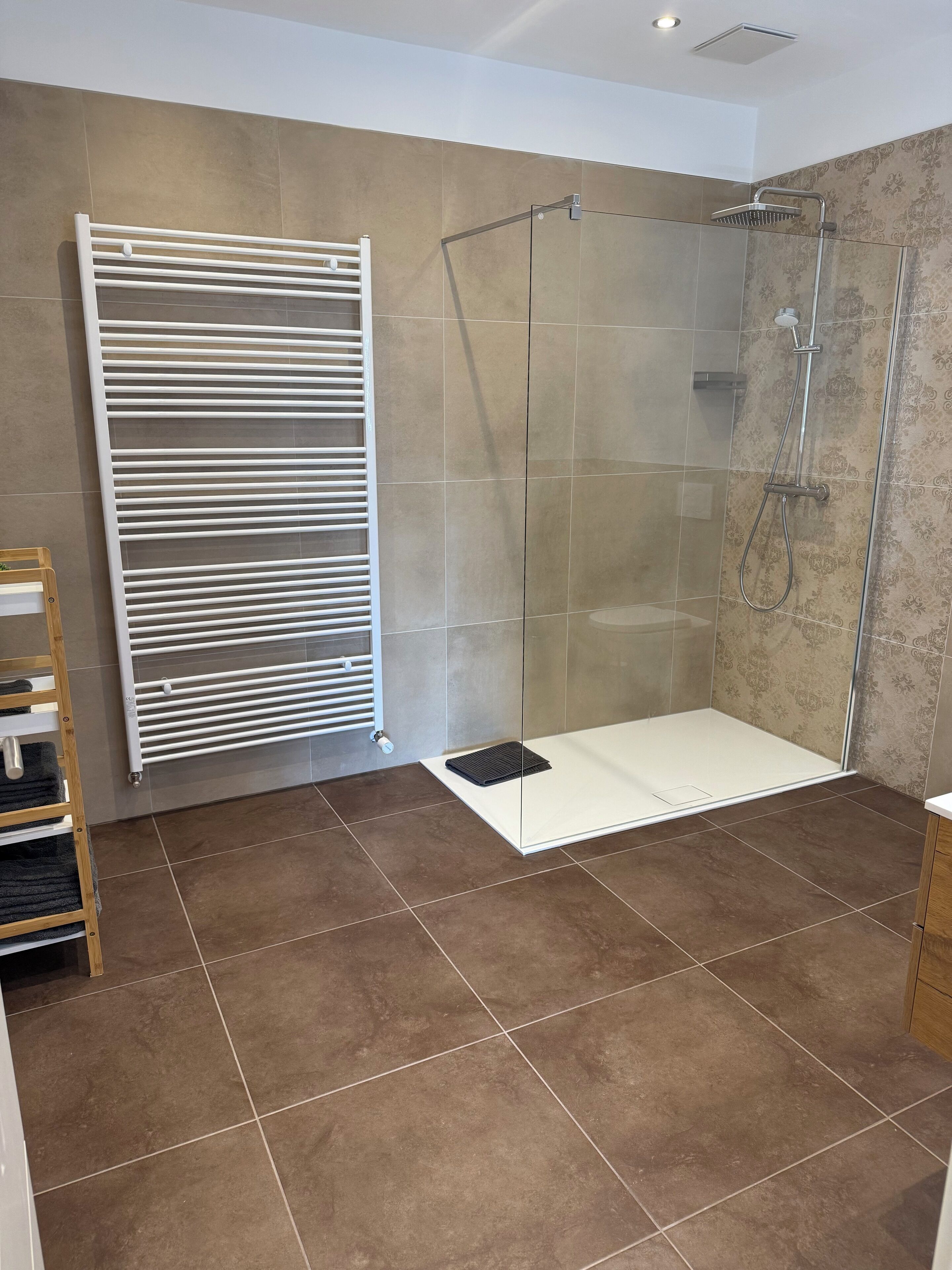 Un baño moderno con cabina de ducha de vidrio, un perchero blanco y un perchero de madera.