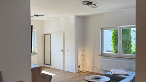 A spacious living area with a wooden floor, a grey sofa, a round coffee table, and a dining table with chairs.