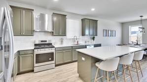 A modern kitchen with a central island, stainless steel appliances, and light wood flooring. - South Austin Luxe Boho House 4BR 2.5BA With SPA, Pool & EV Charger (Mustang Ridge)