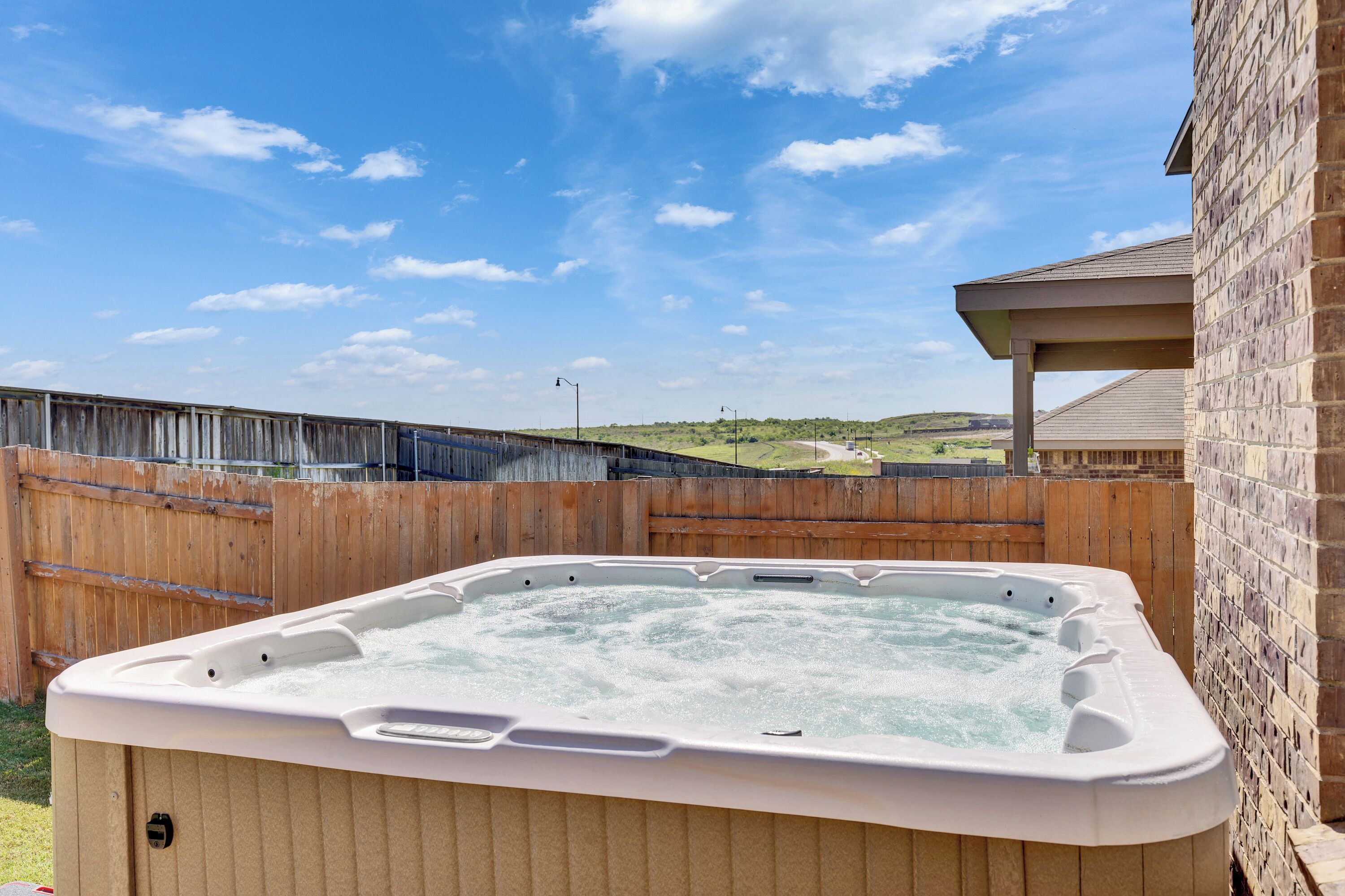 A hot tub in a backyard with a wooden fence and a brick wall.