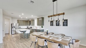A modern kitchen with stainless steel appliances, a dining area with a long table and wicker chairs, and a hanging light fixture. - South Austin Luxe Boho House 4BR 2.5BA With SPA, Pool & EV Charger (Mustang Ridge)