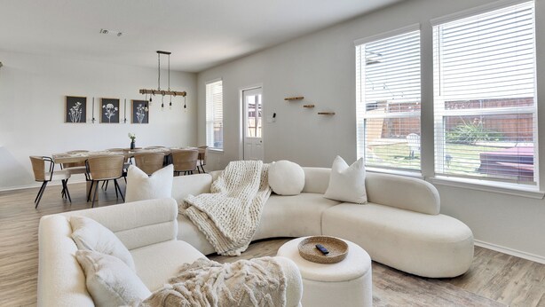 A spacious living room with a large white sectional sofa, a dining area with a wooden table and chairs, and large windows with blinds. - South Austin Luxe Boho House 4BR 2.5BA With SPA, Pool & EV Charger (Mustang Ridge)