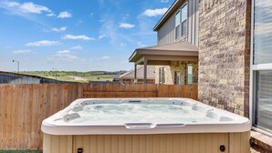 A hot tub in a backyard with a wooden fence, a brick wall, and a house in the background. - South Austin Luxe Boho House 4BR 2.5BA With SPA, Pool & EV Charger (Mustang Ridge)