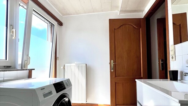 Une cuisine moderne dotée d’un lave-linge encastré, d’un plafond en bois et offrant une vue sur l’extérieur.