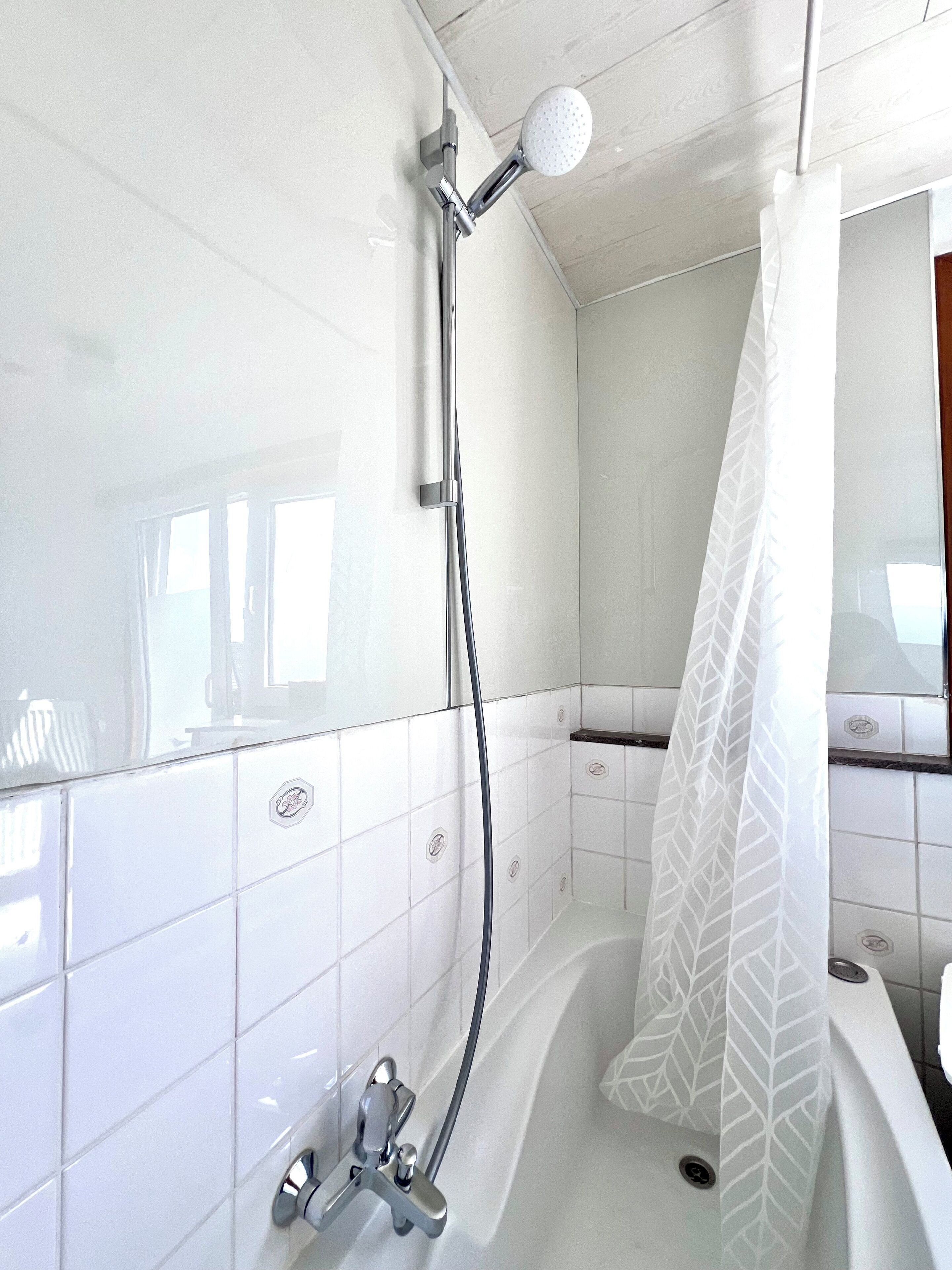 A modern bathroom with white tiles, a shower with a handheld showerhead, and a bathtub with a shower curtain.