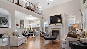 Un salón espacioso con pisos de madera, chimenea, televisor grande y balcón.