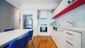 Une cuisine moderne avec des meubles blancs, un plancher en bois et un coin repas doté de chaises bleues.