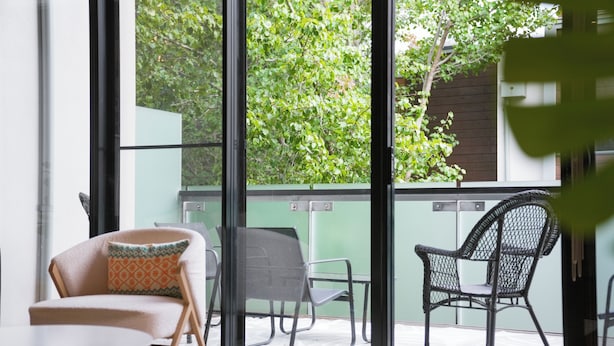 Il s’agit d’un espace intérieur moderne doté d’une porte vitrée donnant sur une zone extérieure. À l’intérieur, on trouve deux chaises et une petite table.