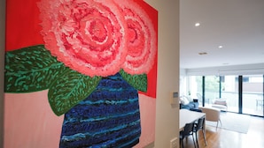 Un intérieur moderne agrémenté d’un grand tableau abstrait au mur, d’un coin repas avec des chaises et une table, et de grandes fenêtres laissant entrer la lumière naturelle.
