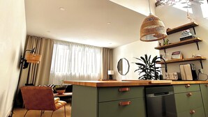 A modern kitchen with a central island, wooden flooring, and a dining area with a chair and table. - Stylish Two-Level Apartment with Private Rooftop Terrace – Downtown Montreal (Montréal)