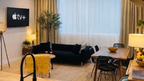 A modern living room with a black sofa, a dining table, and a kitchen area with a sink. - Stylish Two-Level Apartment with Private Rooftop Terrace – Downtown Montreal (Montréal)